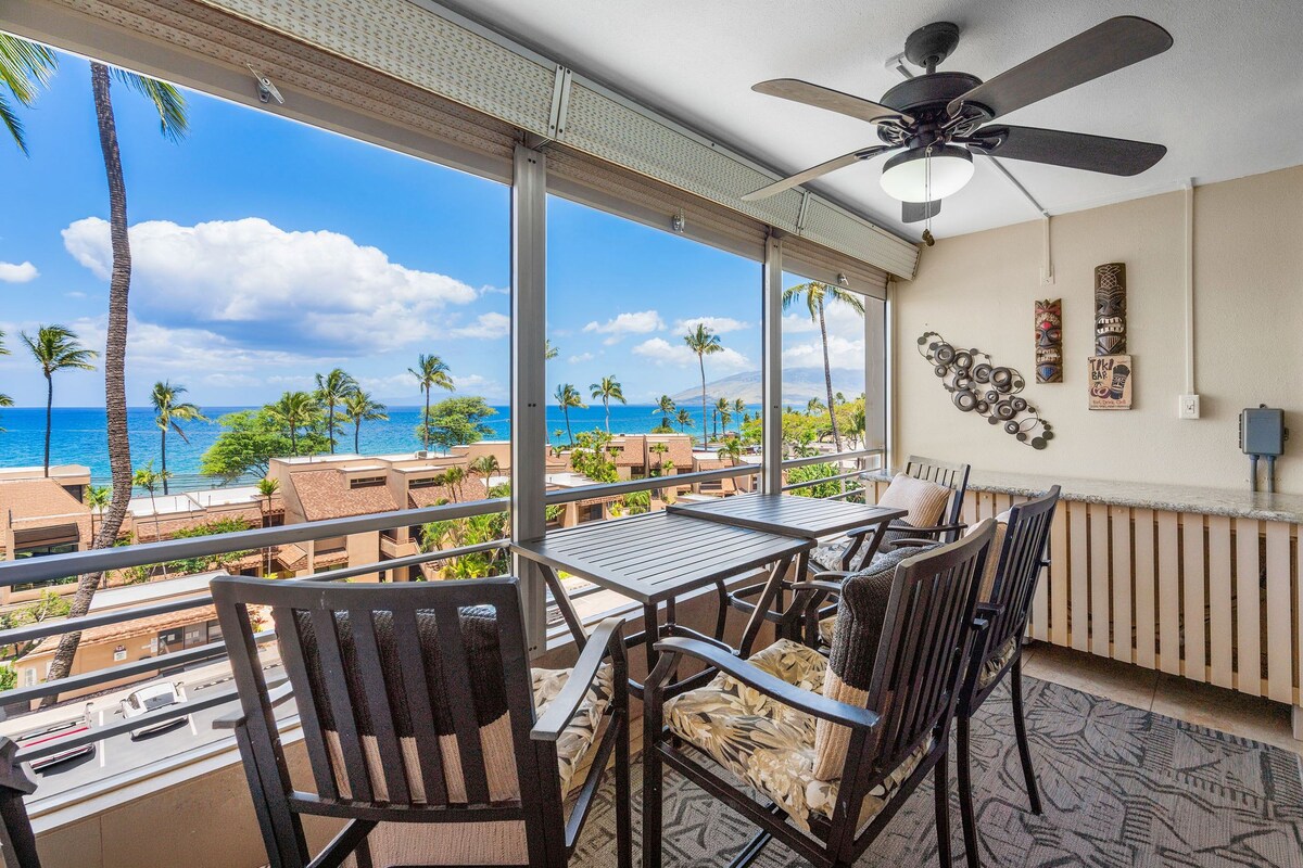 Ein Balkon mit Tisch und Stühlen, der Blick auf einen Strand mit Palmen und dem Meer freigibt.