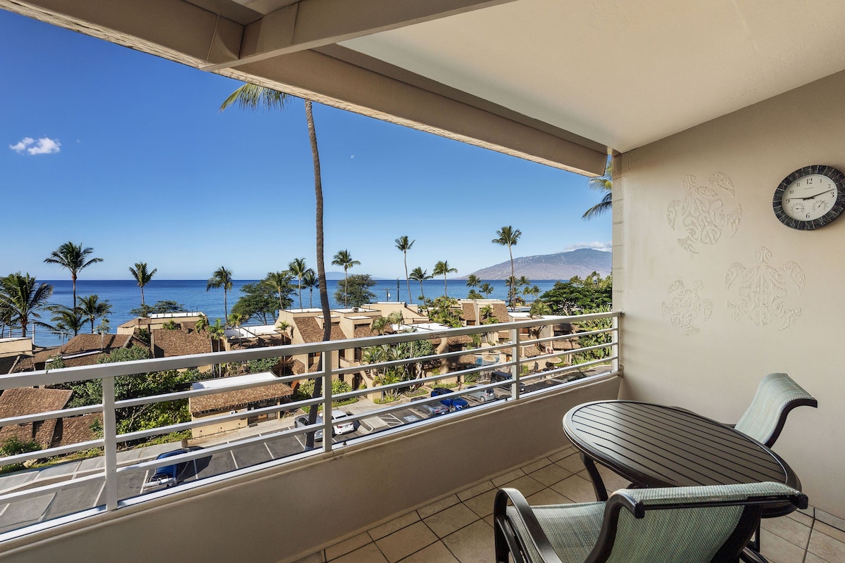 A balcony with a view of the ocean, palm trees, and a clock on the wall.
