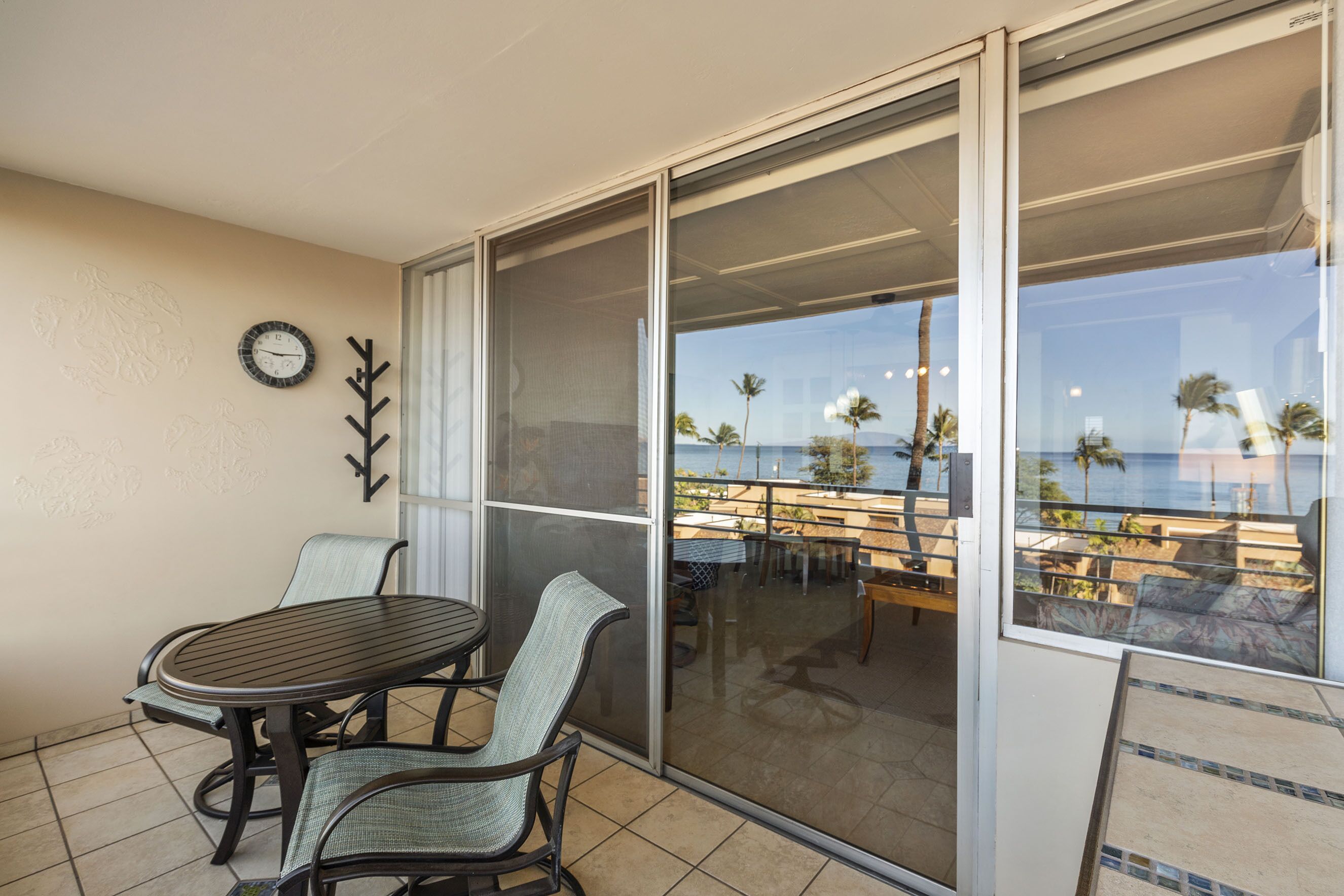 Ein Balkon mit Tisch und Stühlen, einer Uhr und Blick auf den Strand und Palmen.