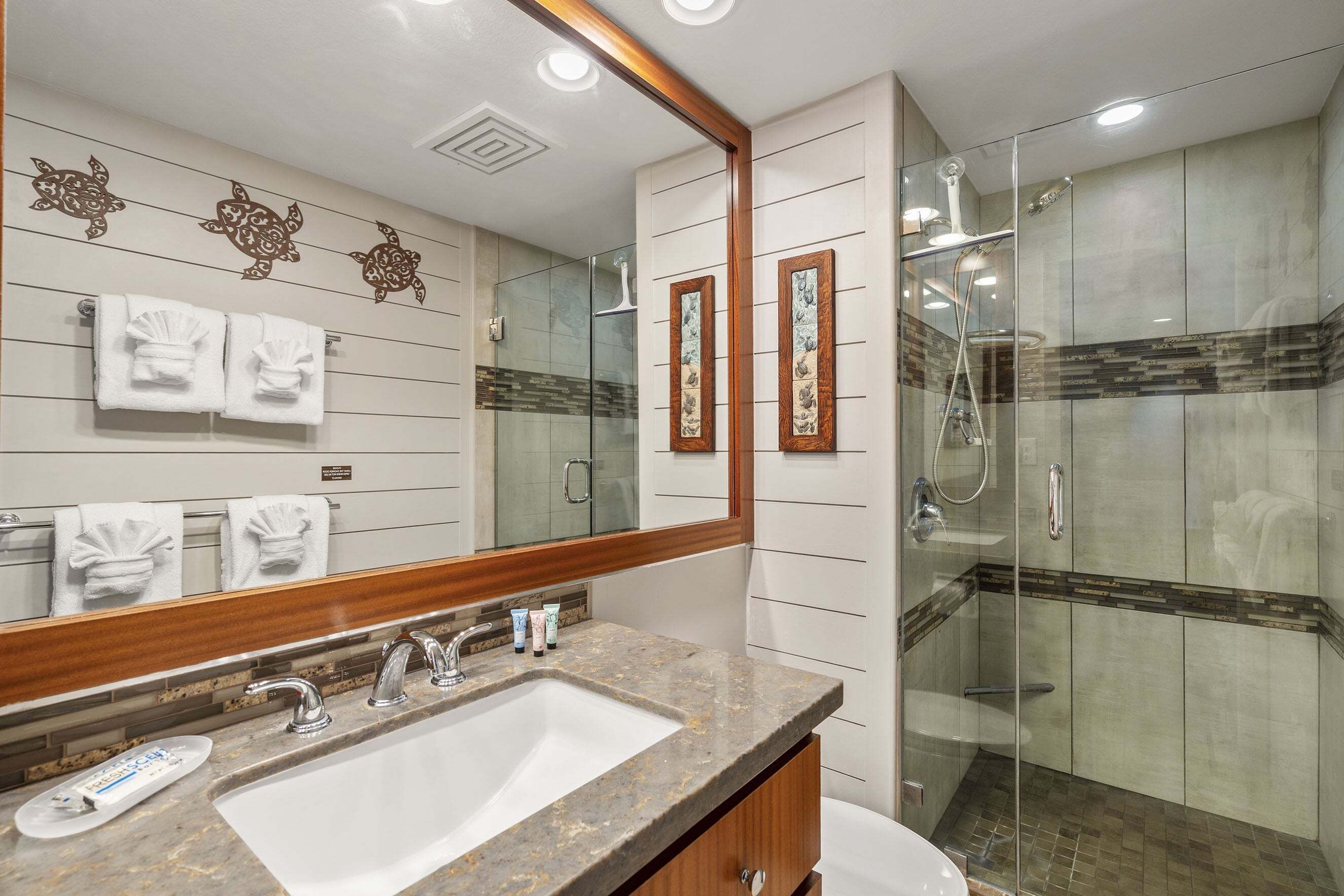 A bathroom with a sink, mirror, towel rack, shower, and decorative wall tiles.