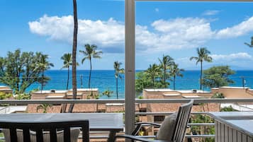 A balcony with a view of the ocean, palm trees, and buildings.