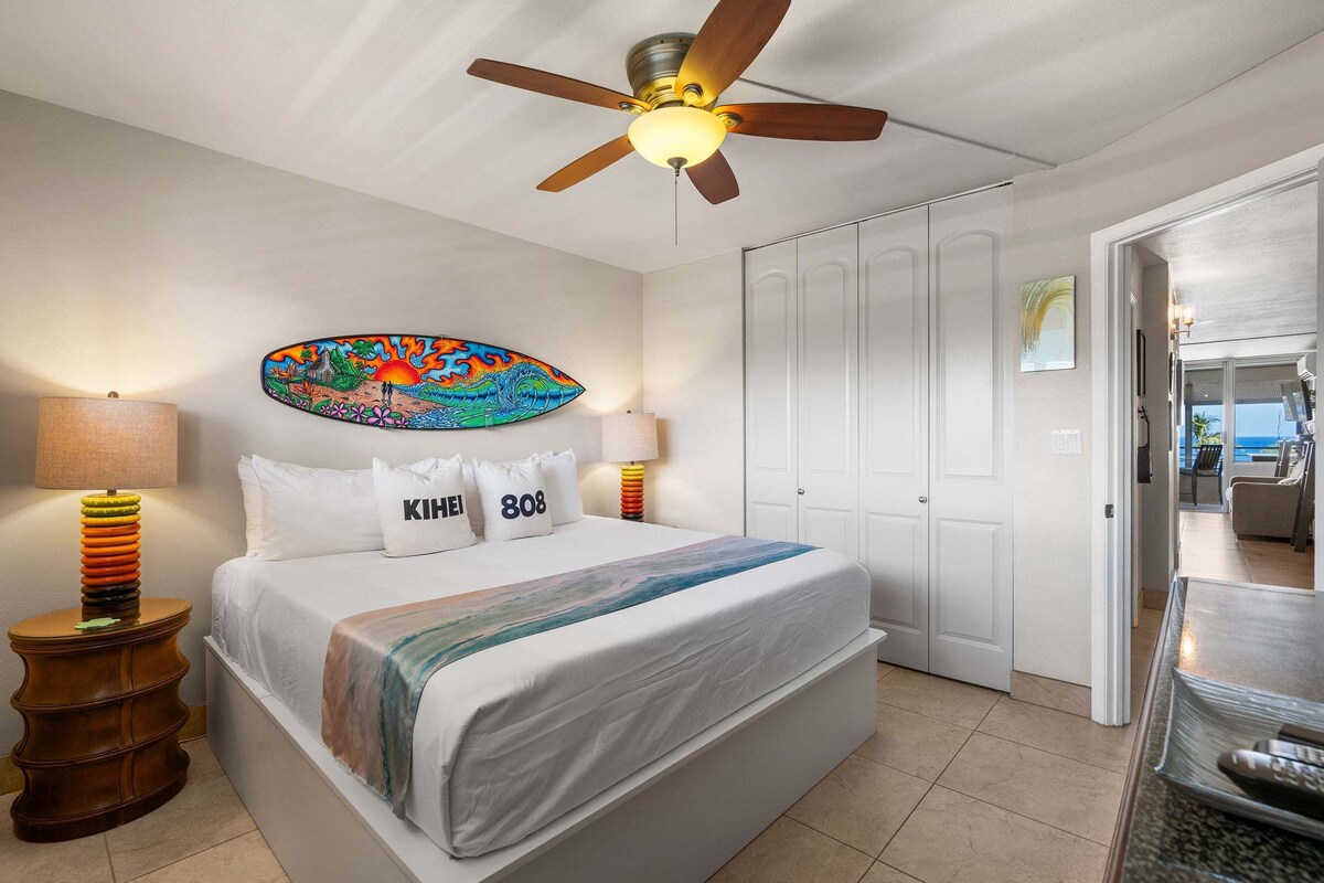A bedroom with a bed, a ceiling fan, a wall art piece, and a door leading to another room.