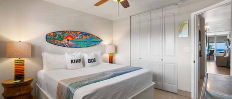 A bedroom with a bed, a ceiling fan, a wall art piece, and a door leading to another room.