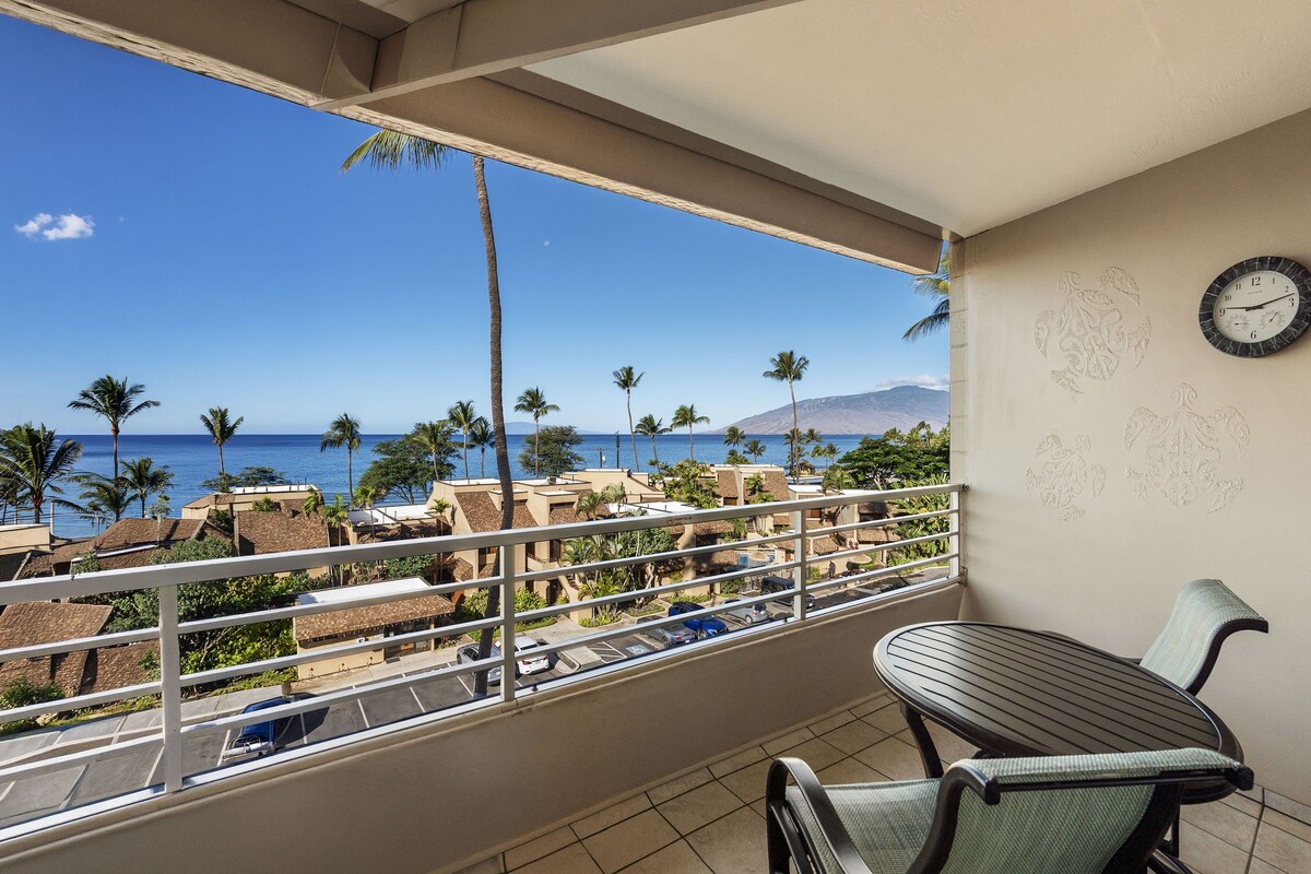 A balcony with a view of the ocean, palm trees, and a clock on the wall.