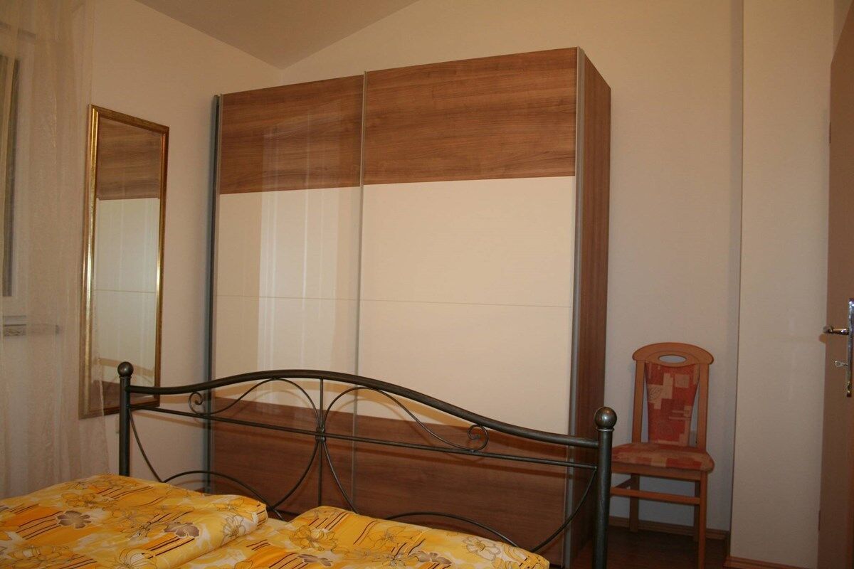 Een slaapkamer met een bed, een houten garderobe, een stoel en een spiegel.