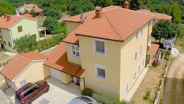 Um edifício de vários andares com telhado de telhas vermelhas, rodeado por vegetação e céu claro.