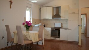 Uma cozinha compacta com armários brancos, um fogão e uma pia. Há uma mesa de jantar com cadeiras e um vaso de flores.