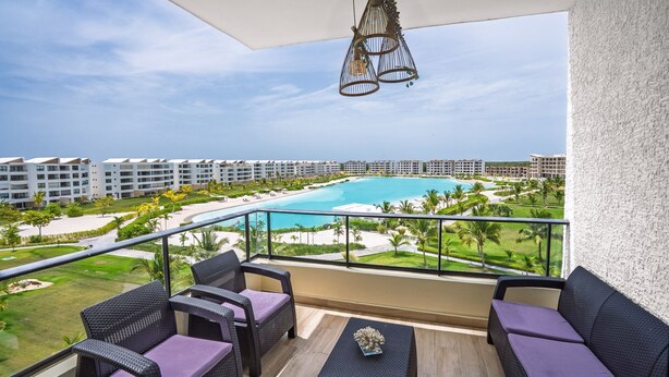 Un balcone con mobili in vimini, vista su una piscina e edifici circostanti.