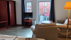 A hotel room with a bed, a sofa, a TV, and a balcony with a view of a brick building. - Pension Hafenblick - Rooms with city view (Barth)
