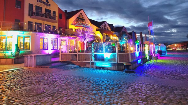 A waterfront area with buildings, including a restaurant named "SUR LA MER" and a sign for "Aperito". - Pension Hafenblick - Rooms with city view (Barth)