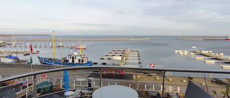 Une terrasse avec deux chaises et une table donnant sur une marina, où l’on peut admirer des bateaux et un quai.