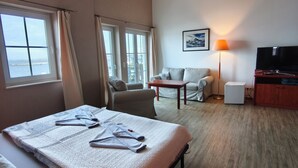 A hotel room with a bed, a sofa, a TV, and a table. - Pension Hafenblick - Zimmer mit Balkon Hafenblick (Barth)