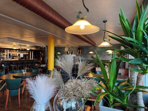 L’intérieur d’un restaurant, avec un espace bar, des chaises vertes et des plantes décoratives.