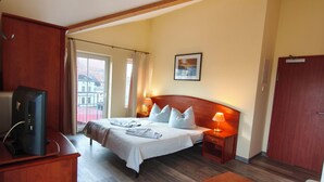 A hotel room with a bed, bedside tables, a desk with a computer, and a view of buildings outside. - Pension Hafenblick - Zimmer mit Balkon 3 (Barth)