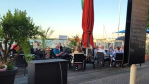 An outdoor seating area with tables and chairs, a flag, and a chalkboard menu. - Pension Hafenblick - Zimmer mit Balkon 3 (Barth)