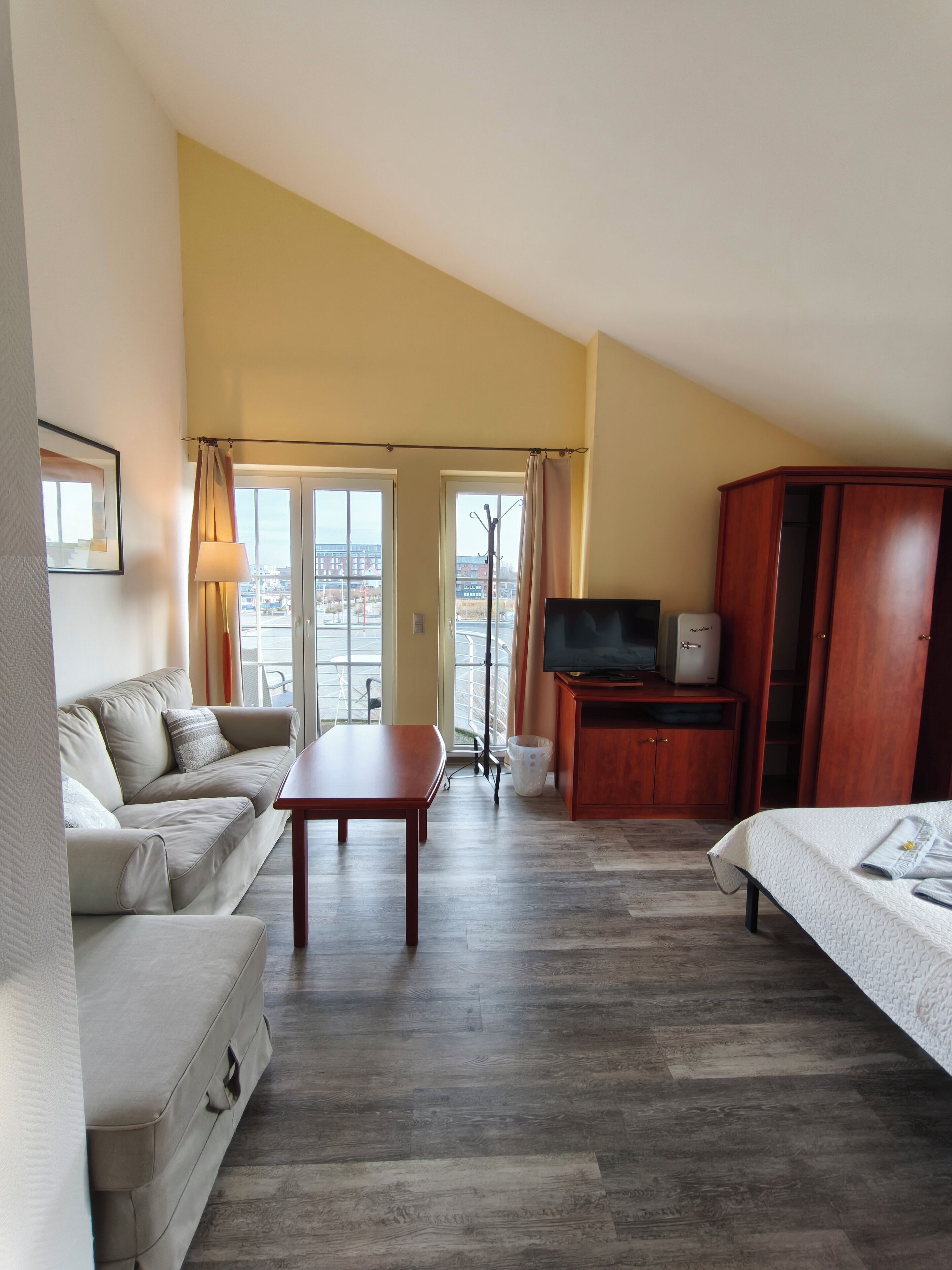 Een hotelkamer met een sofa, een tafeltje, een televisie, een kledingkast en een bed.