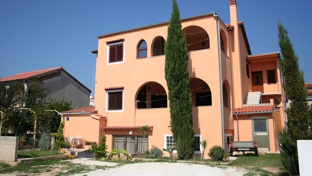 Un bâtiment à deux étages, doté d’un toit plat, de fenêtres en arc de cercle et d’une cheminée centrale.