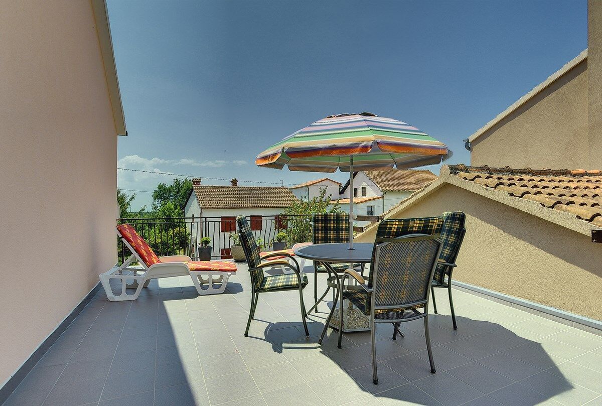 Un balcone con tavolo e sedie, un ombrellone a righe e vista sulle case vicine.
