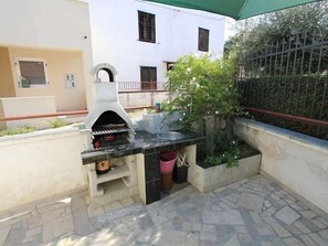 An outdoor kitchen area with a stone-tiled floor, a built-in grill, and a small sink. - Casa Bella (16076-K1) - Pomer (Pomer)