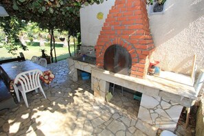 Um pátio externo com forno de tijolos, piso de pedra e mobiliário branco.