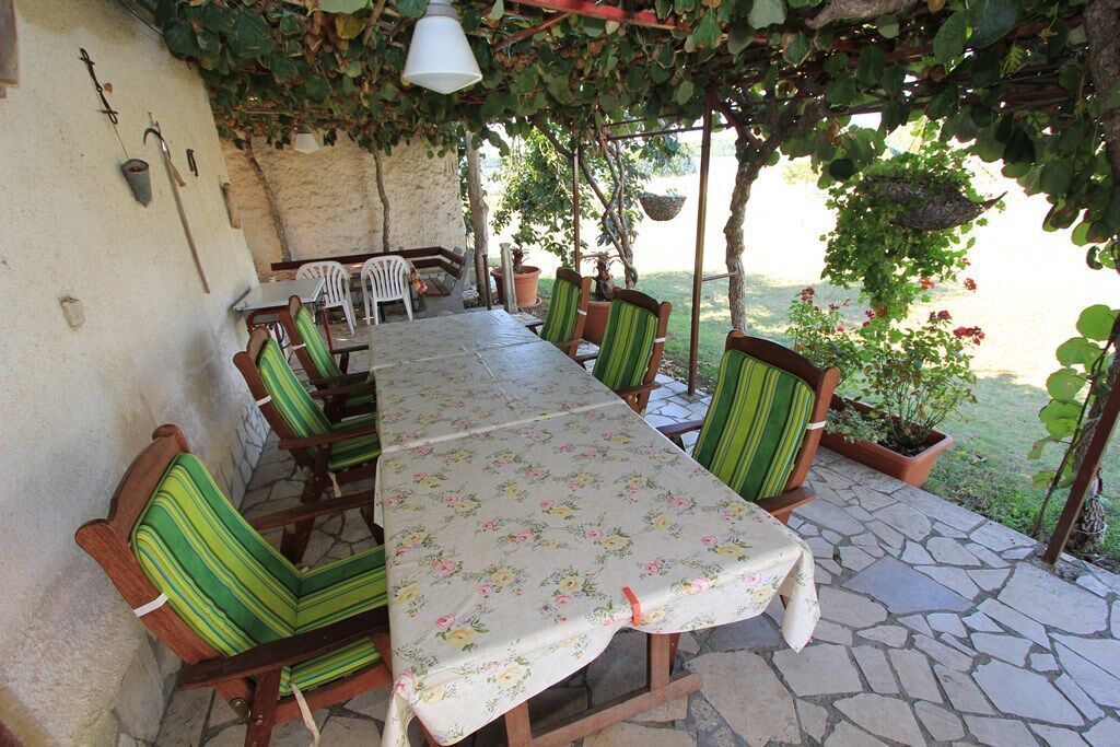 Un'area pranzo all'aperto riparata, con tavolo e sedie, circondata da piante in vaso e un pavimento in pietra.