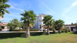 Un edificio bianco con un cortile centrale, circondato da palme e siepi curate.
