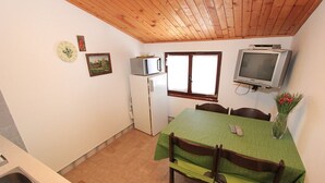Una cucina compatta con microonde, frigorifero e una piccola finestra. Un tavolo da pranzo con sedie è posizionato sotto un soffitto in legno.