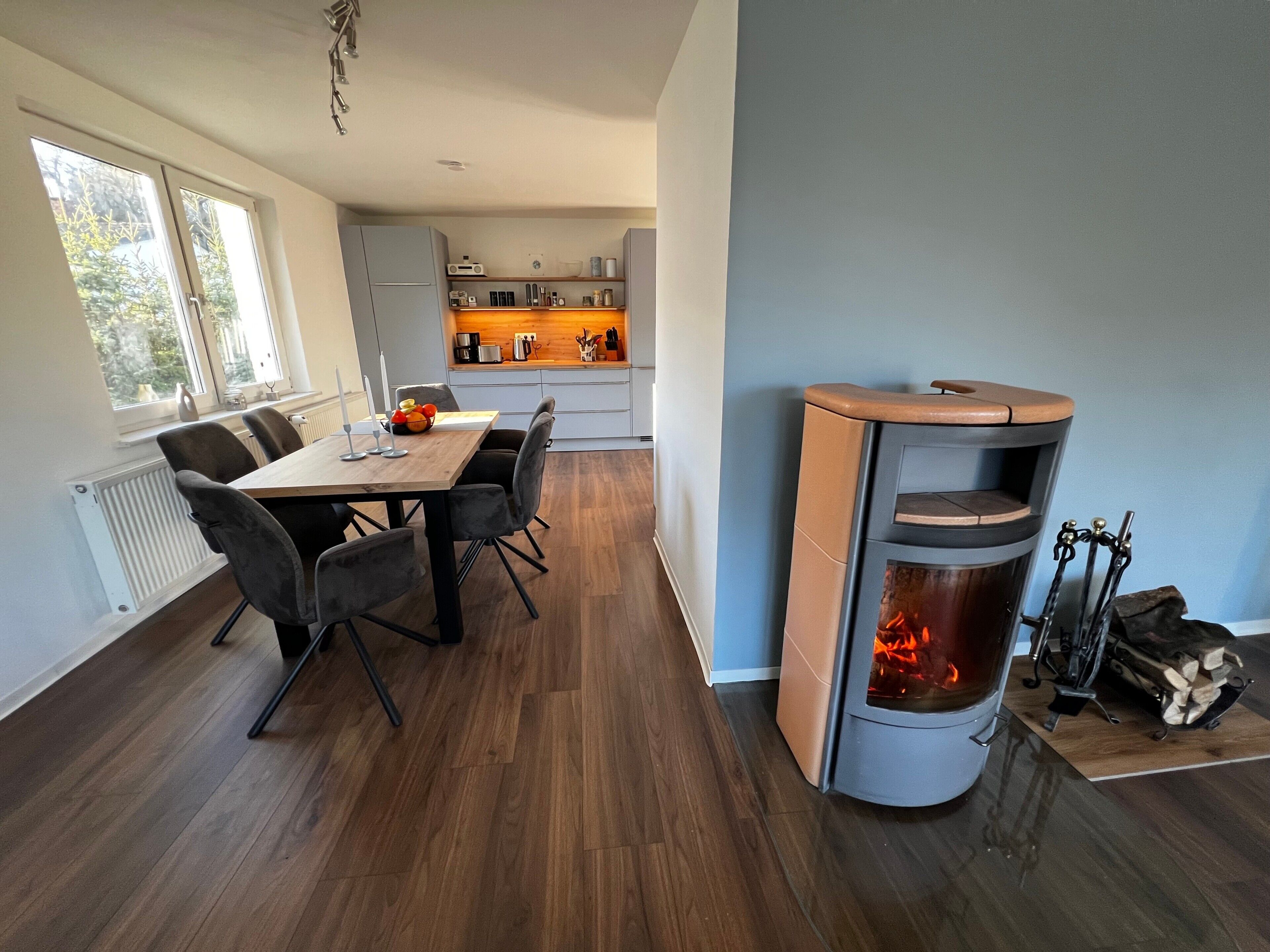 Eine moderne Küche mit Einbauherd, ein Essbereich mit Holztisch und Stühlen sowie ein großes Fenster, das für natürliches Licht sorgt.