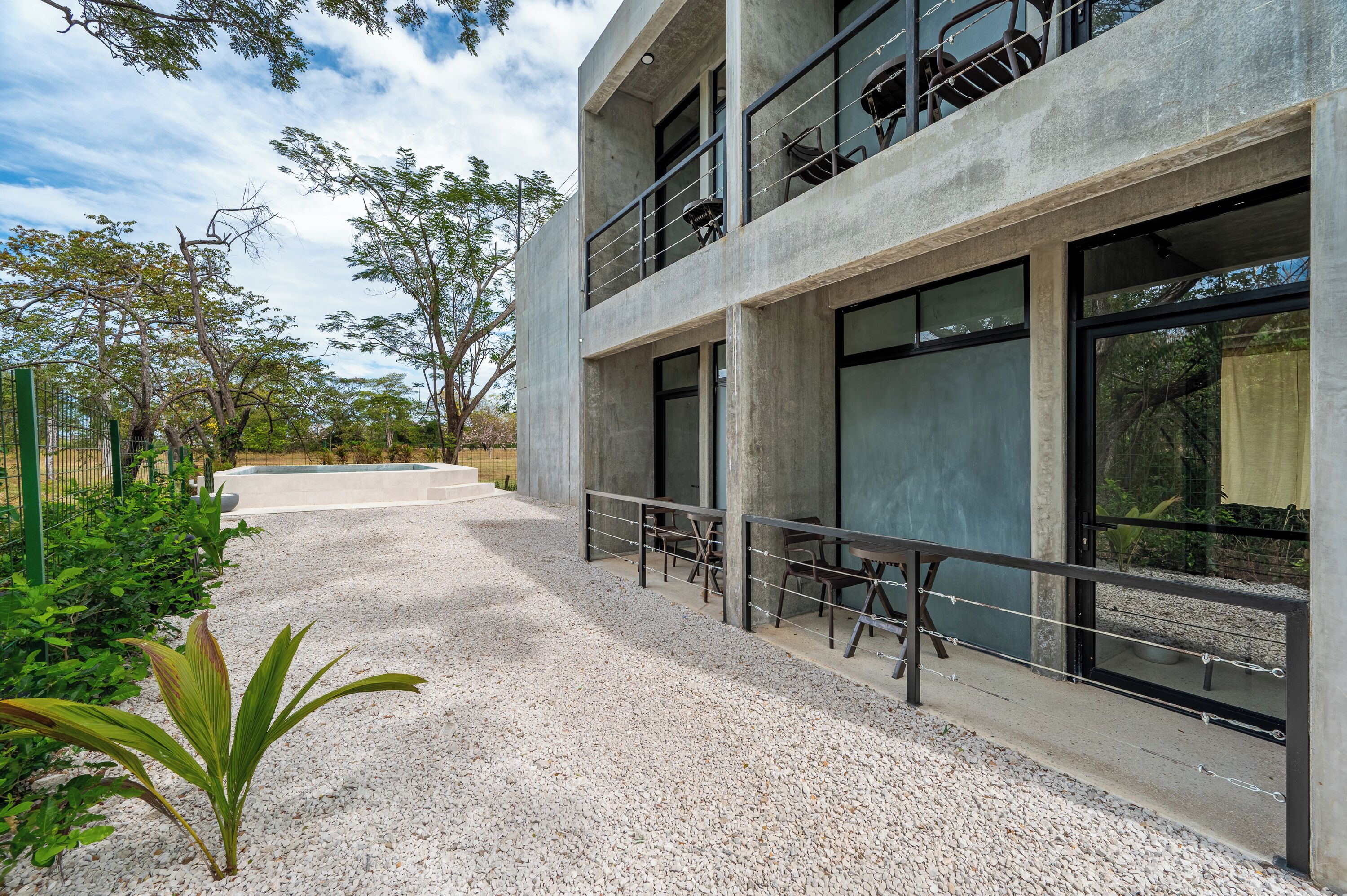 Un edificio moderno con fachada de hormigón, ventanas amplias y zona de estar exterior con mesas y sillas.