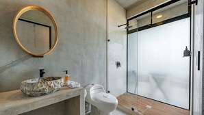 A modern bathroom with a concrete sink, a round mirror, and a glass shower enclosure. - NELBLU FLAMINGO SUITES (Playa Flamingo)
