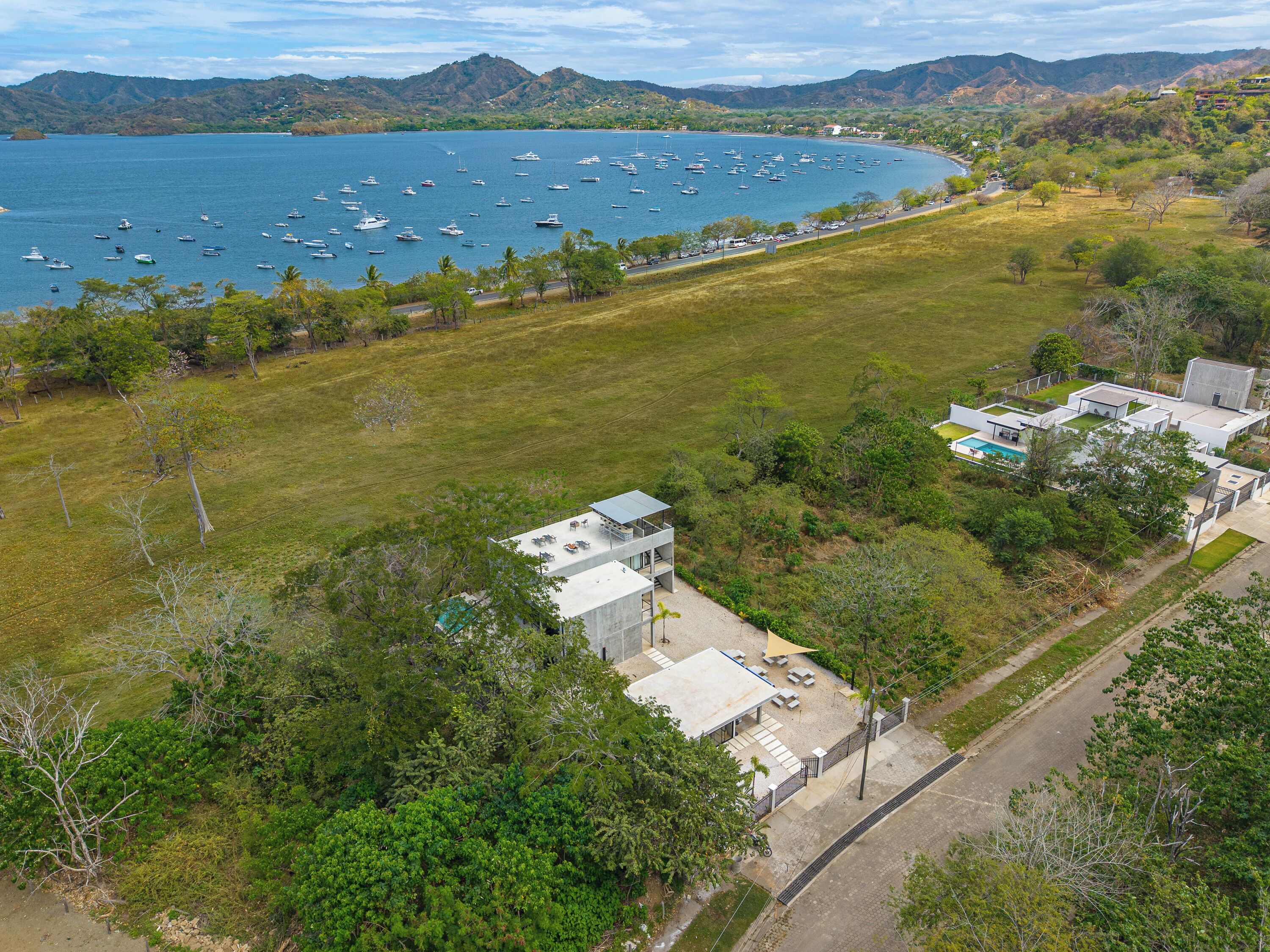 A coastal property with a large grassy area, a swimming pool, and a view of the sea with boats.