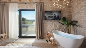 Une salle de bain moderne avec une baignoire sur pieds, une grande fenêtre avec des rideaux, un mur en pierre et un tableau accroché.