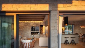Un intérieur moderne avec un mur en pierre, un plancher en bois, un canapé blanc, un coin repas et une cuisine équipée de tabourets.