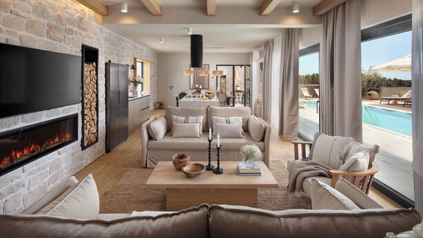 Un salon moderne avec une cheminée, un ensemble de canapés, une table basse agrémentée d’objets décoratifs et une vue sur une piscine.