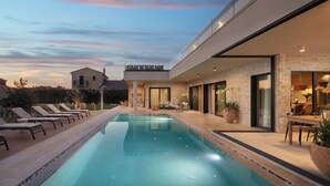 Une maison moderne dotée d’une piscine, d’un espace salon extérieur et d’une façade en pierre.