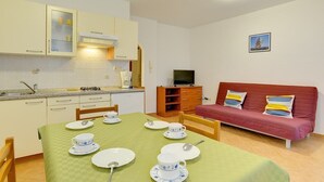 A compact kitchen with a dining area, a red sofa, and a television. - Apartments Ulika (16031-A2) - Medulin (Medulin)