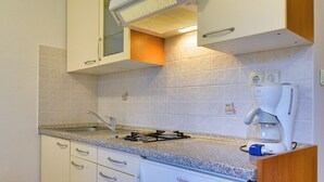 A compact kitchen with white cabinets, a gas stove, a coffee maker, and a tiled backsplash. - Apartments Ulika (16031-A2) - Medulin (Medulin)
