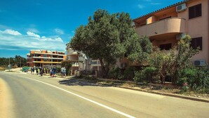 A multi-story building with balconies, a clear sky, and a tree-lined street. - Apartments Ulika (16031-A2) - Medulin (Medulin)