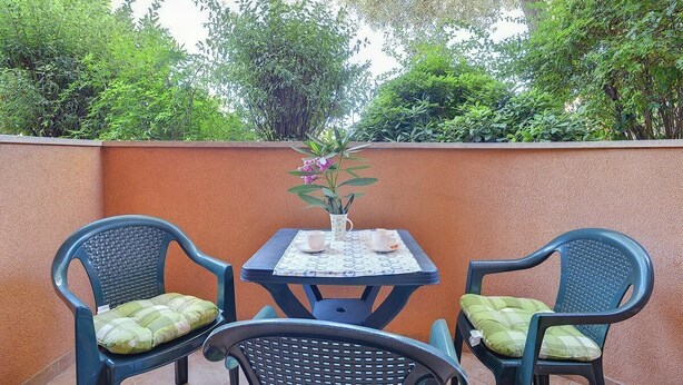 An outdoor seating area with two chairs and a table, surrounded by a low wall and lush greenery. - Apartments Ulika (16031-A2) - Medulin (Medulin)
