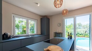 A modern kitchen with a central island, large windows, and a view of a swimming pool. - CASA LIMONAIA - Where the sea speaks to you and silence embraces your soul (Rapallo)