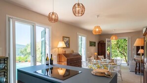 A modern kitchen with a large island, dining area with white chairs, and a view of greenery outside. - CASA LIMONAIA - Where the sea speaks to you and silence embraces your soul (Rapallo)