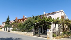 Um imóvel residencial com portão fechado, muro de pedra e jardim com diversas plantas.