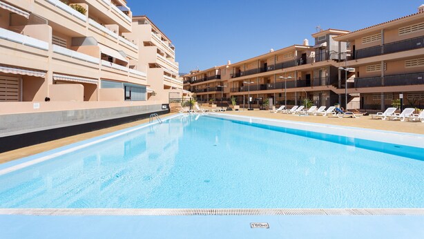 A swimming pool with lounge chairs and a multi-story building with balconies. - Nice sea & pool view apt in Los Cristianos (Los Cristianos)