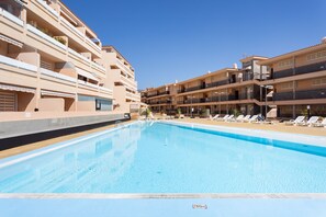 En swimmingpool med solstolar och en flervåningsbyggnad med balkonger.