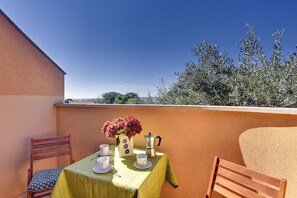 A table set with cups, saucers, a vase with flowers, and a coffee pot on a balcony with a view of trees and a building. - Apartments Ulika (16031-A6) - Medulin (Medulin)