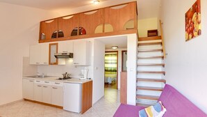 Ein kompakter Wohnbereich mit einer Küchenzeile, einem violetten Sofa und einer Treppe zu einer erhöhten Ebene.