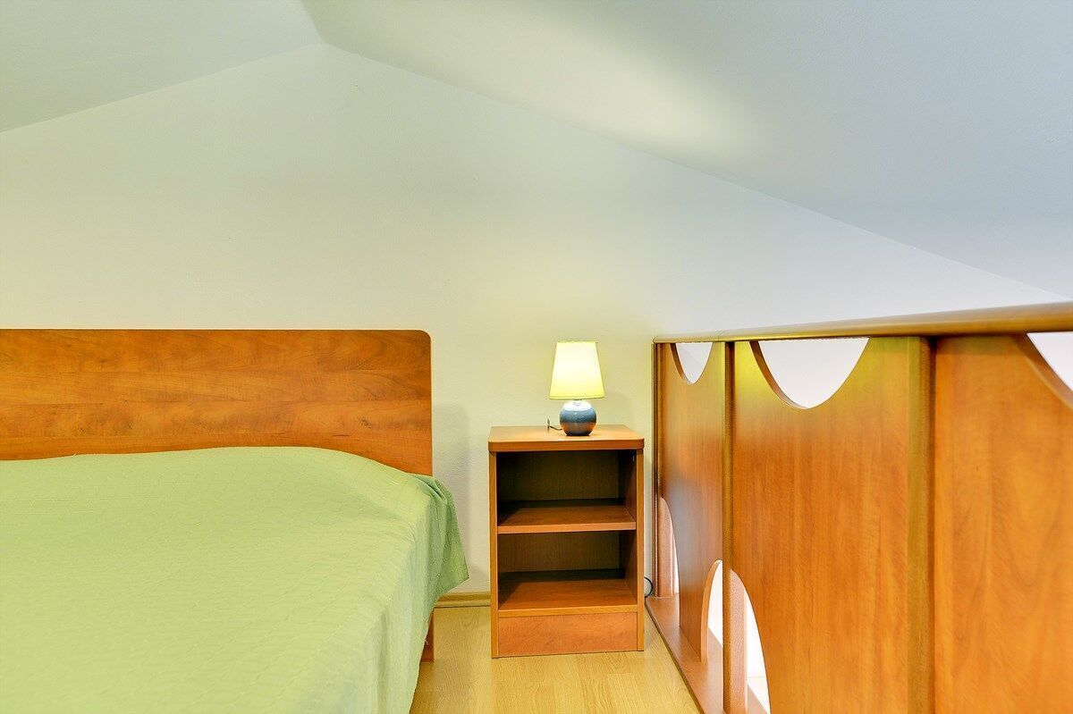 A bedroom with a wooden headboard, a green bedspread, a nightstand with a lamp, and a wooden wardrobe.