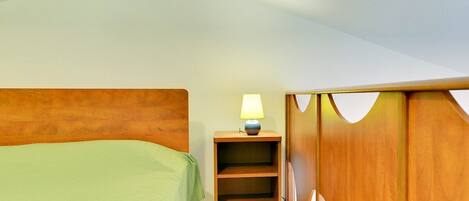 A bedroom with a wooden headboard, a green bedspread, a nightstand with a lamp, and a wooden wardrobe.