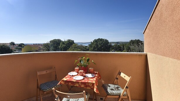 Ein Balkon mit Tisch für zwei Personen, Stühlen und einem Blumentopf.