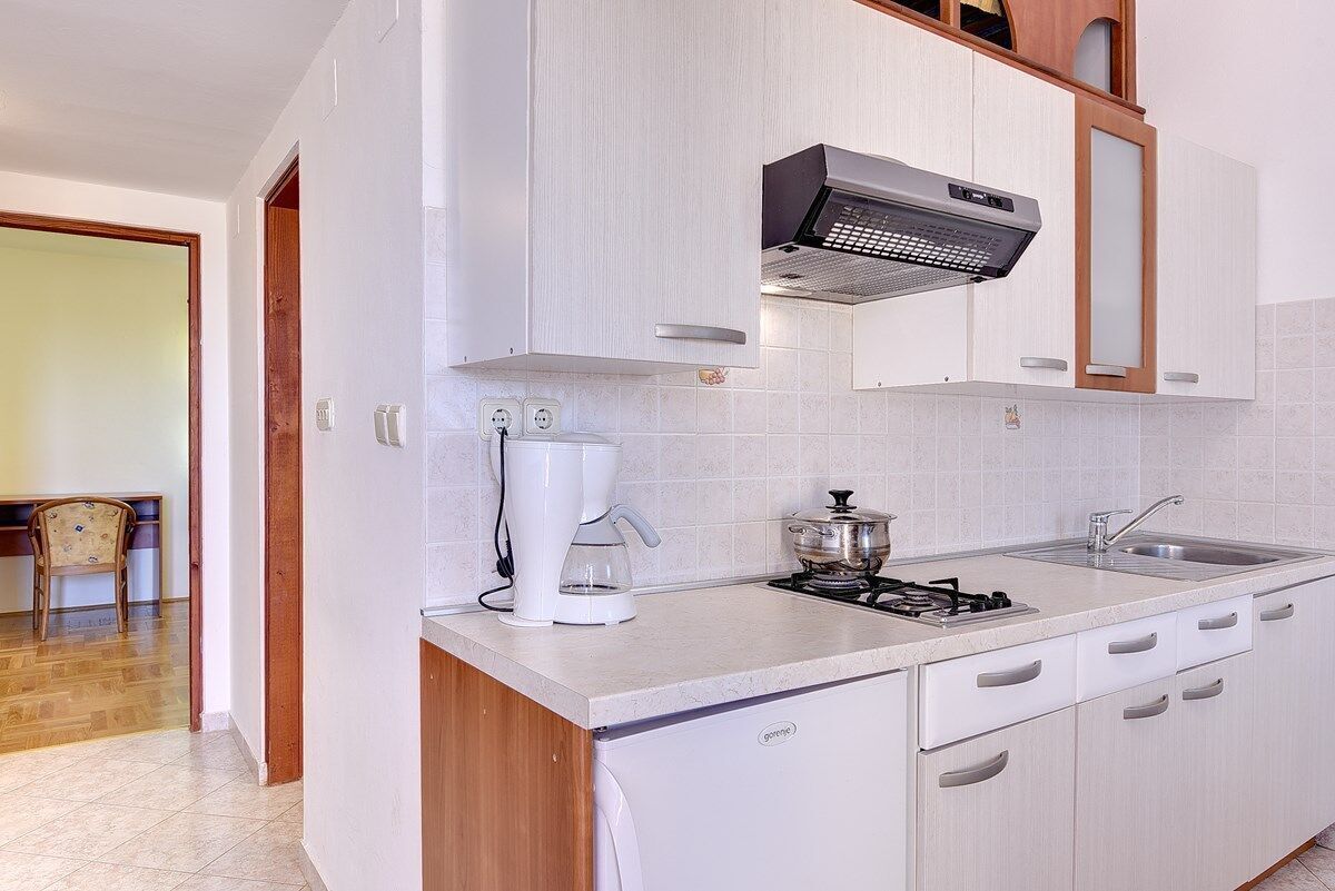 Una cocina moderna con armarios blancos, estufa integrada, cafetera y microondas.